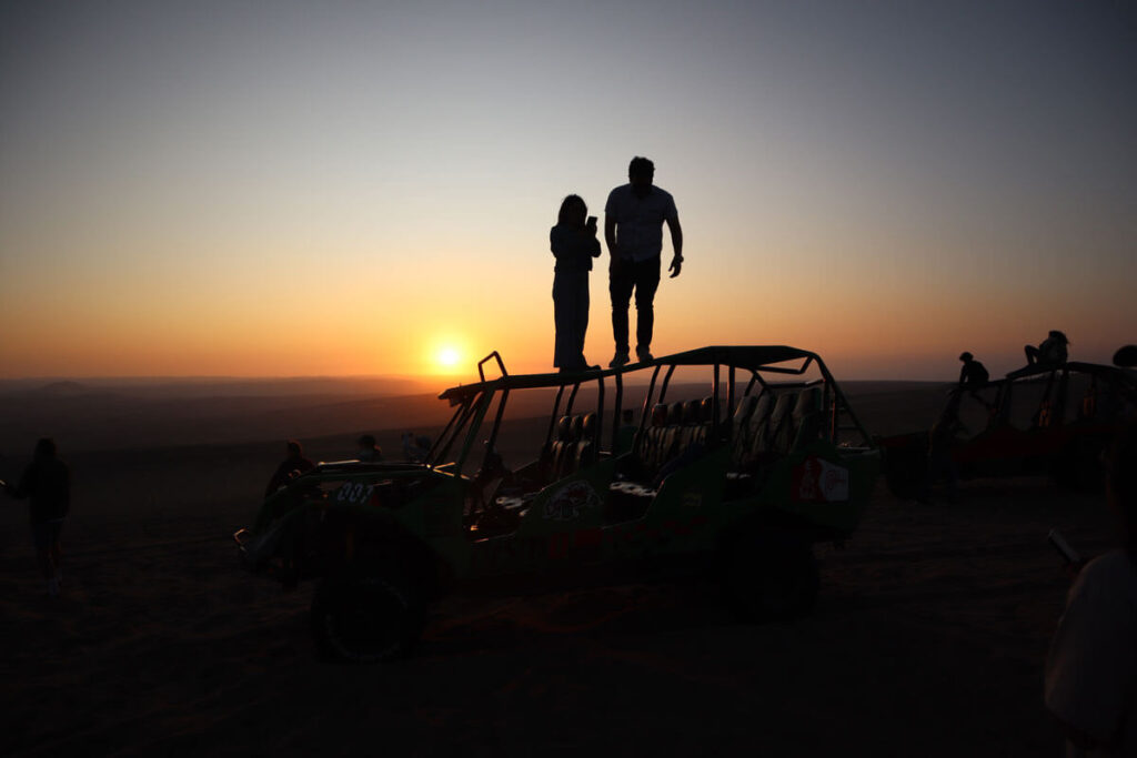 Silhouet van twee mensen staand op een buggy met zonsondergang